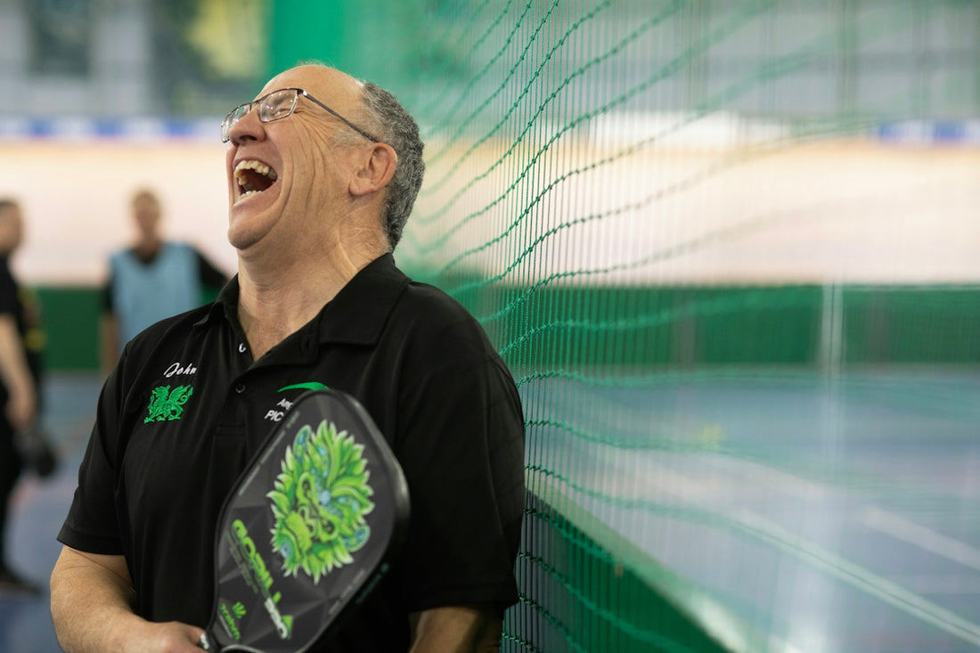 The man is laughing with a pickleball paddle
