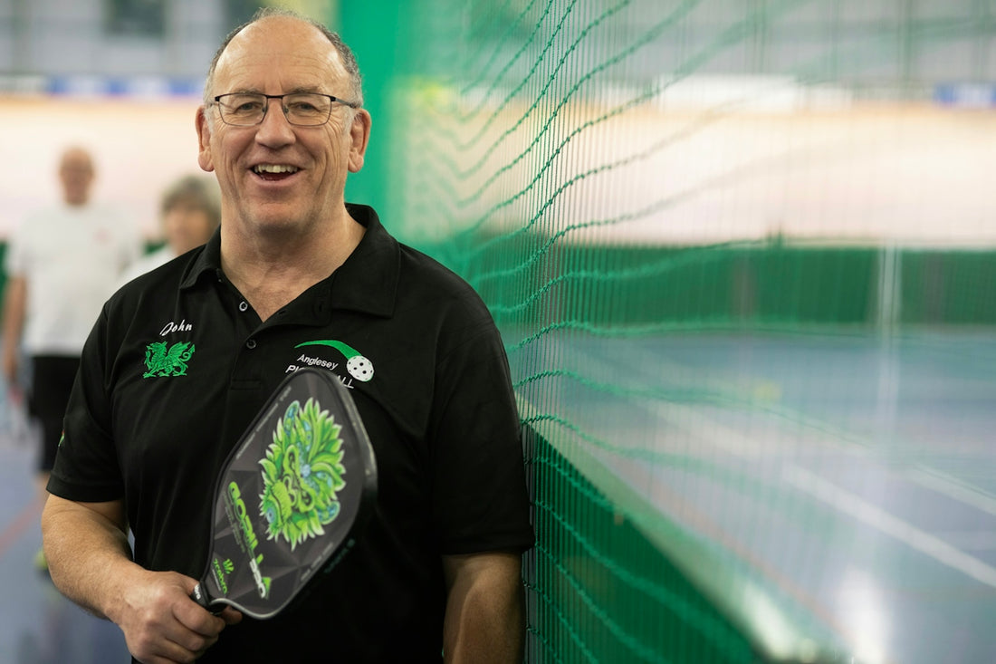A smiling man holds a pickleball paddle