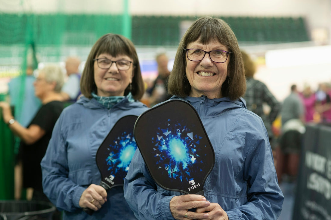 Twins smile, holding pickleball paddles